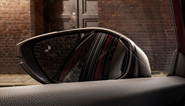 Interior closeup of the door mirror with the reflection of a car in it and a lit up blind spot indicator light.