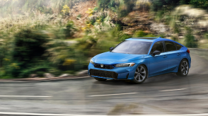 3/4 front view of blue Hatchback taking a turn on a tropical forest highway.
