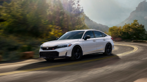 3/4 front view of white Civic Si taking a turn on a mountain highway.
