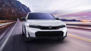 Front view of white Civic Si driving toward camera on a mountainous oceanside highway.