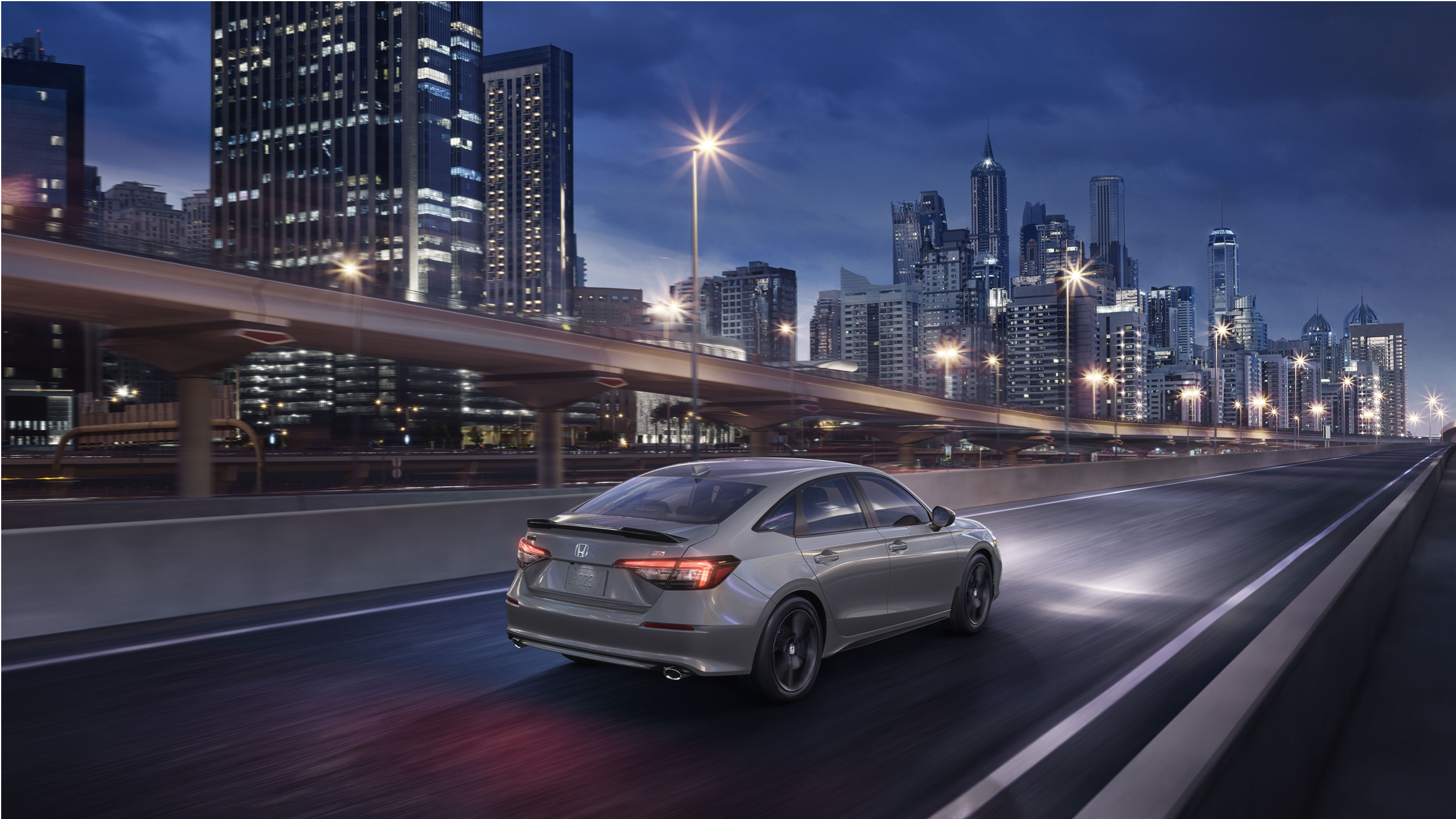 3/4 bird’s eye side view of a grey Civic Si driving on highway overlooking a city.