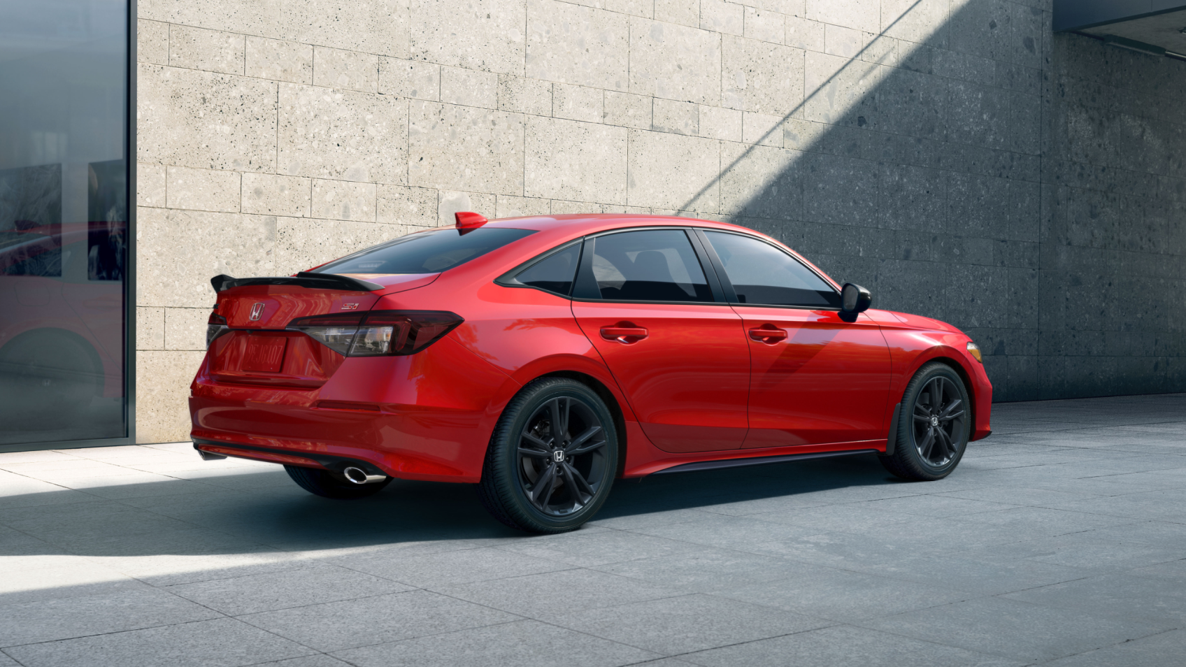 Rear side view of a red Civic Si parked in front of a stone-walled building.