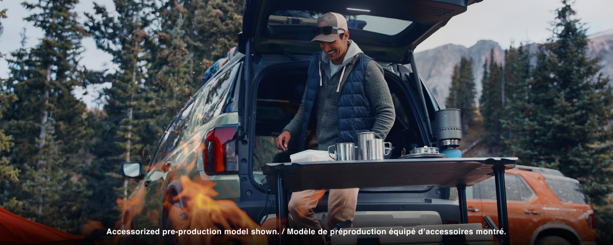 A man sets up a camping cookout behind a Passport. 