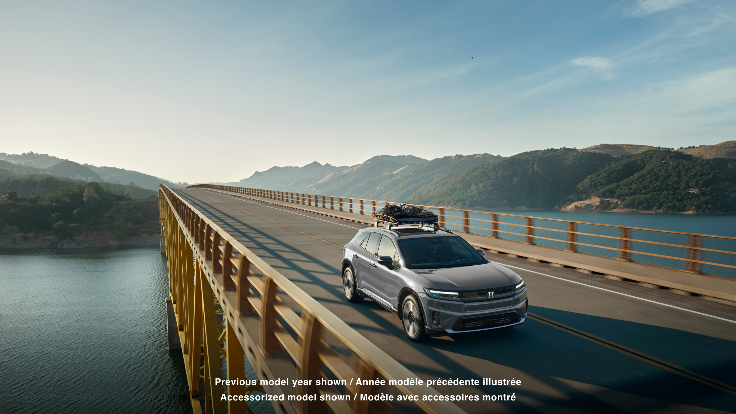 Wide 3/4 front view of grey Prologue with cargo on the roof rack driving over a bridge.