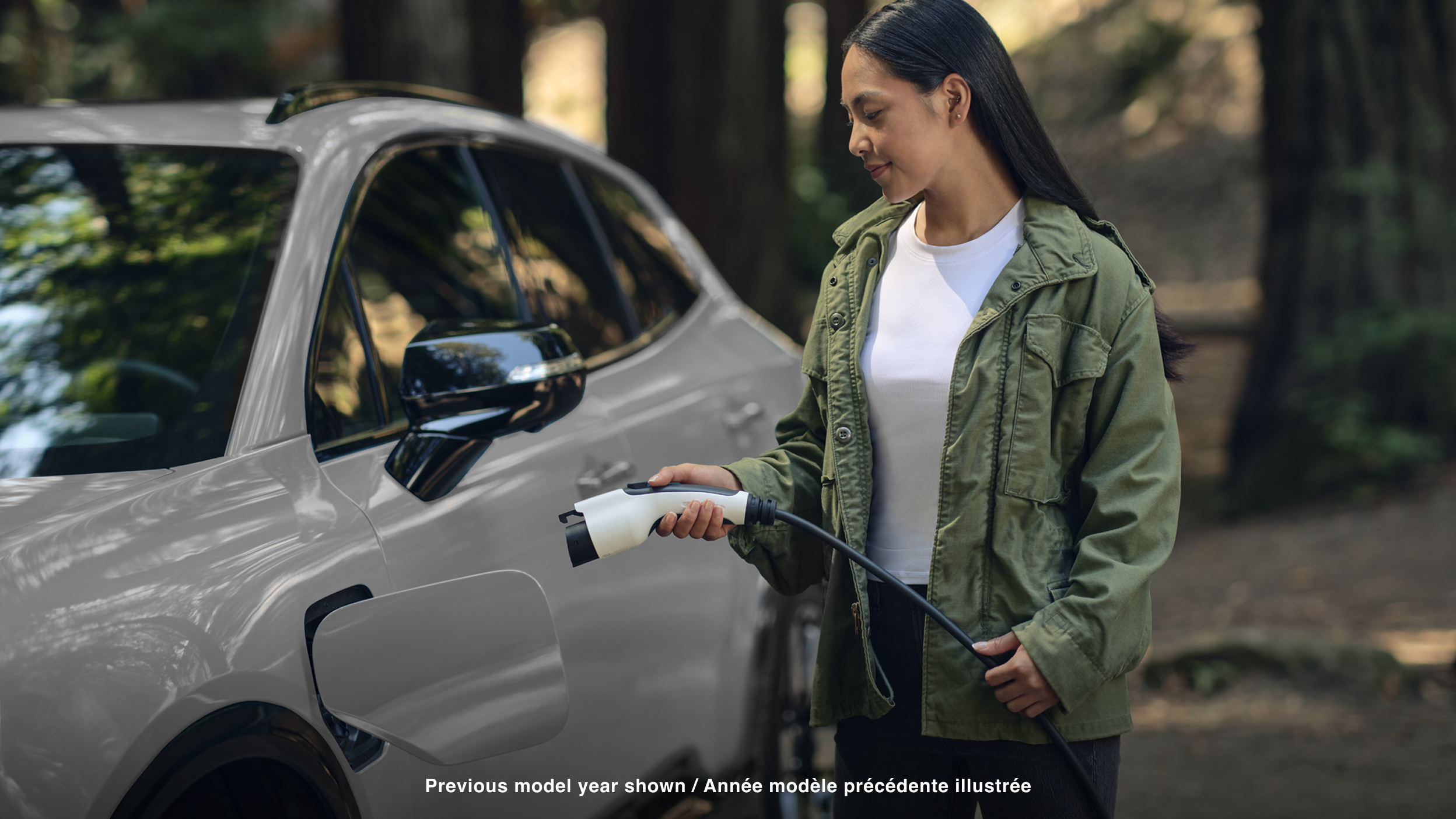 View of a woman plugging in a charging cord into a white Prologue in temperate forest.