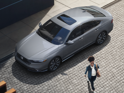 3/4 bird’s eye view of woman walking away from a grey Accord parked curbside in an upscale urban setting.