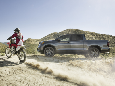 Side view of grey Ridgeline on desert hills with motocrosser on the left.