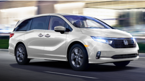 3/4 side front view of white Odyssey driving on city street at night.