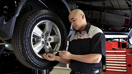 Image of a Honda technician using equipment to check and maintain tire pressure on a black Honda in a workshop setting. // Image d'un technicien Honda utilisant un équipement pour vérifier et maintenir la pression des pneus d'une Honda noire dans un atelier.